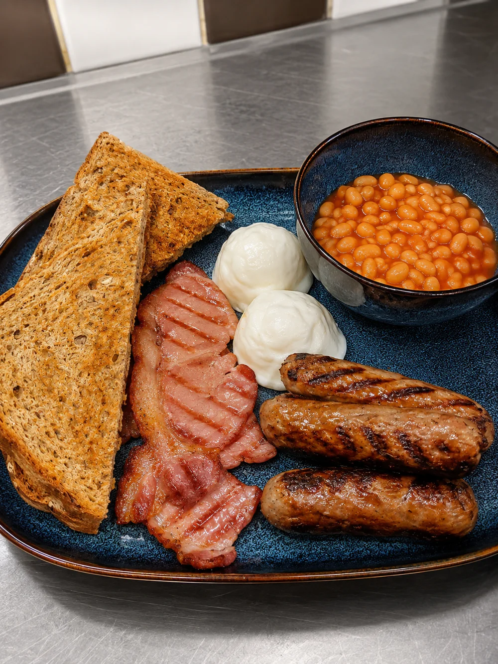 A full breakfast plate with toast, bacon, sausages and beans